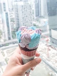 Cropped hand of woman holding ice cream cone by window in city