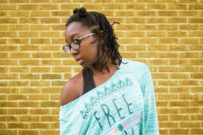 Young woman standing against brick wall