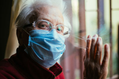 Close-up portrait of senior woman wearing mask with reflection on window