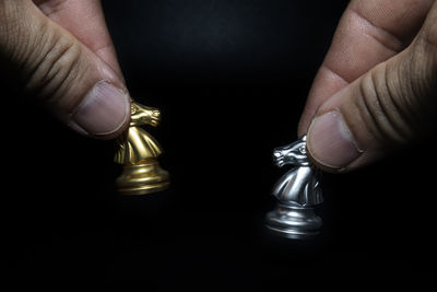 Close-up of hand holding chess against black background