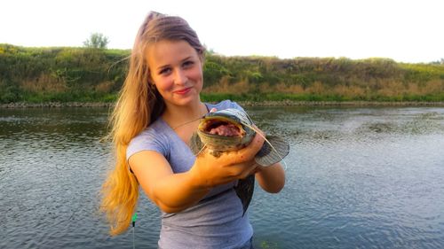 Portrait of young woman holding fish at lakeshore