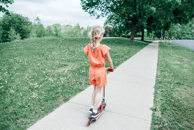 Rear view of girl on push scooter at park