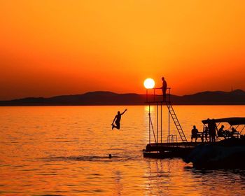 Silhouette people on sea against orange sky during sunset