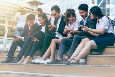 Full length of friends sitting on mobile phone