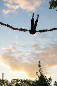 Low angle view of man hanging on rope against sky