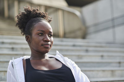 Confident african american female runner sitting on stone stairs on street while relaxing during workout and looking away