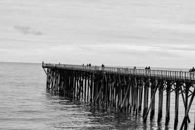 People on pier over sea against cloudy sky
