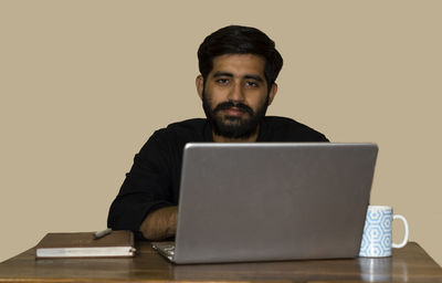 A young indian man looking at camera while working on laptop. selective focus on man's face.