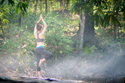 Rear view of teenage girl practicing tree pose in forest