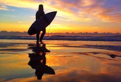 Silhouette of surfer carrying surfboard on beach at sunset