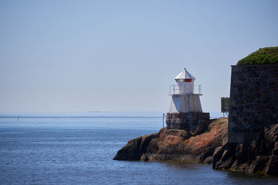 Lighthouse by sea against clear sky