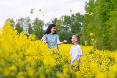 Rear view of woman standing amidst yellow flowering plants on field