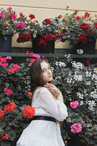 Portrait of young woman standing by flowering plants