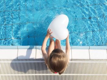 Directly above shot of girl holding balloon while sitting by poolside