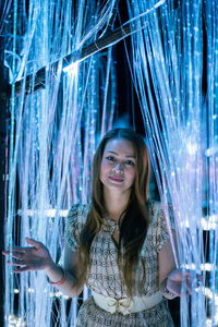 Portrait of young woman standing in illuminated room