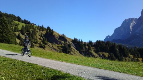 Low angle view of man cycling on mountain road against clear blue sky