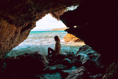 Side view of woman sitting on rocky shore