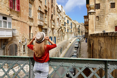 Tourist woman holds hat on iron bridge looking the old town of valletta, malta