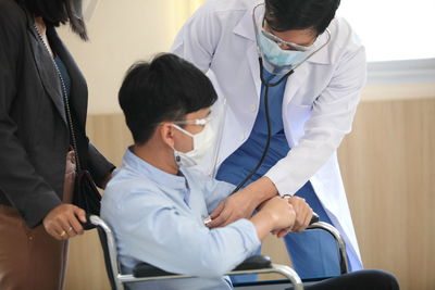 Doctor examining man sitting on wheelchair in hospital