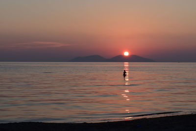 Silhouette person in sea against sky during sunset