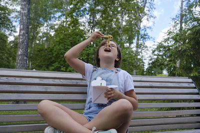 Teenage girl on a walk on a summer day in the park has lunch with noodles wok