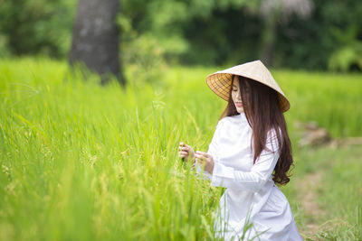 Woman wearing asian style conical hat while kneeling on field