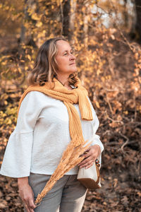 Young woman looking away while standing on autumn leaves