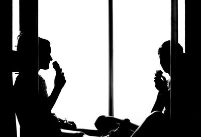 Silhouette women sitting white eating ice cream on doorway