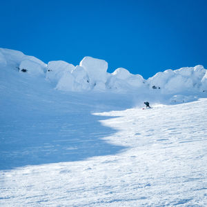 Off piste skier on snow covered snowcapped mountain against blue sky