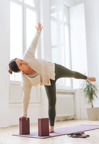 Attractive middle aged brunette woman in sportswear ptactice yoga with equipment in light studio