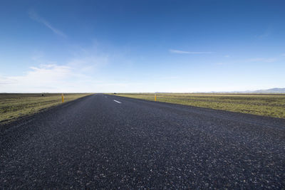 Empty road amidst field against sky