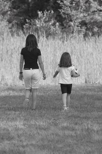 Rear view of mother and girl walking on field