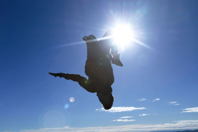 Low angle view of silhouette man jumping with sun shining in sky