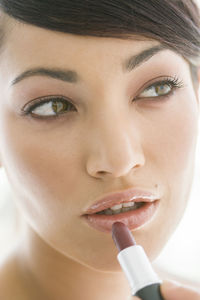 Close-up of beautiful woman looking away while applying lipstick on lips