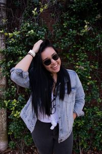 Portrait of smiling young woman with hand in hair standing against ivy