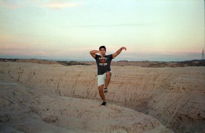 Full length portrait of man with arms raised against sky