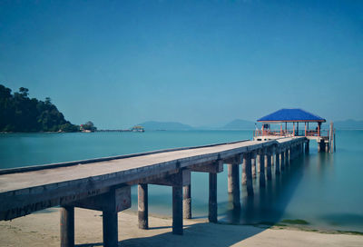 Pier over sea against clear blue sky