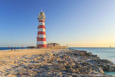 Lighthouse by sea against clear sky