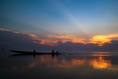 Silhouette people on sea against sky during sunset