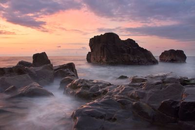 Rocks on shore against sky during sunset