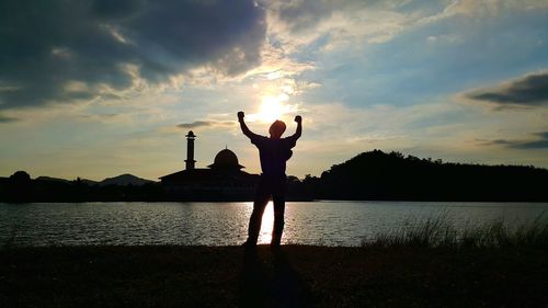Silhouette man standing at lake against sky during sunset