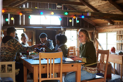 Portrait of young woman using laptop on table while friends enjoying in background at home