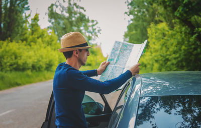 Side view of man reading map standing by car