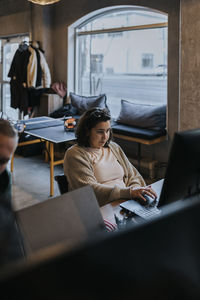 Young female hacker working on laptop by male colleague in startup company