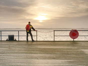 Rear view of man standing by sea against sky during sunset