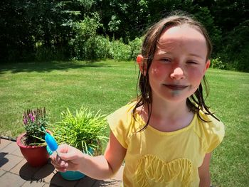 Portrait of smiling girl eating flavored ice while standing against plants in park during sunny day