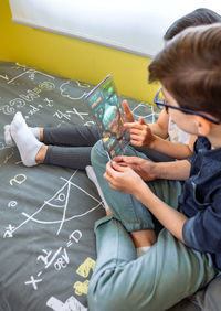 Unrecognizable children playing and having fun with futuristic transparent tablet sitting over bed.
