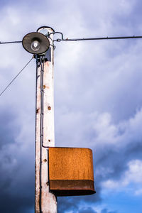 Low angle view of telephone pole against cloudy sky