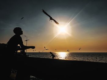 Silhouette birds flying over sea against sky