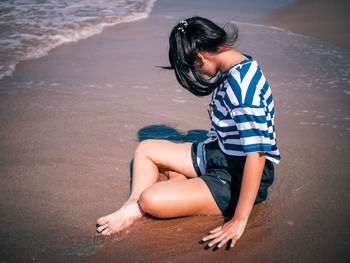 Side view of boy sitting on sand at beach